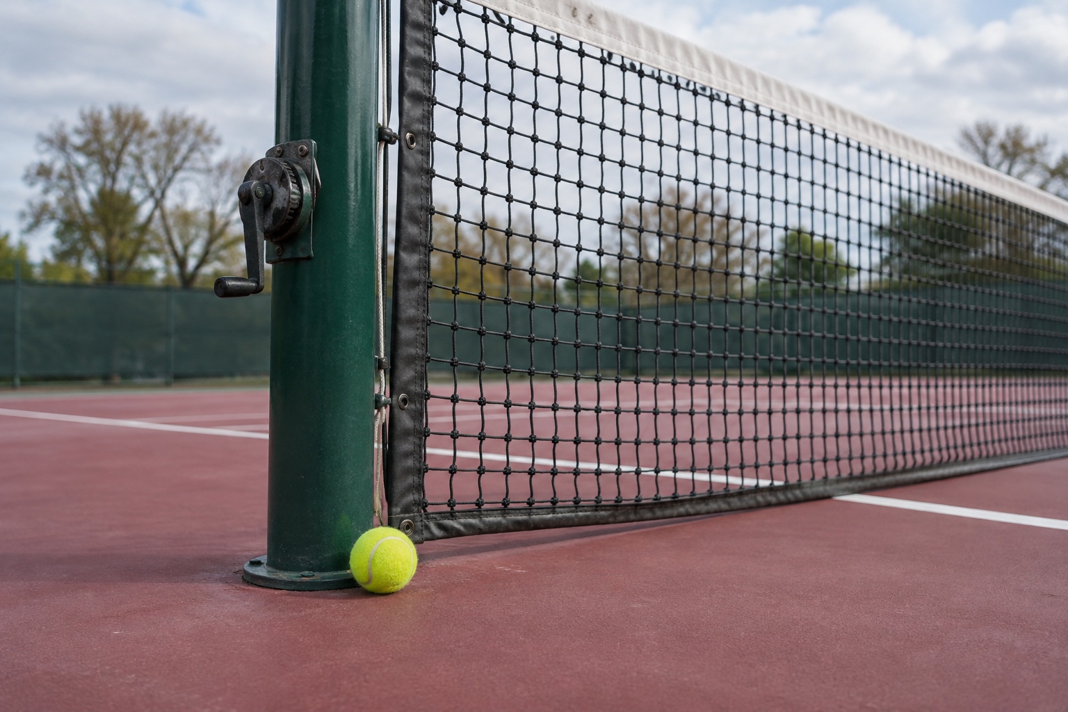 Conceptual illustration of a tennis ball beside a green net post on a hard court.